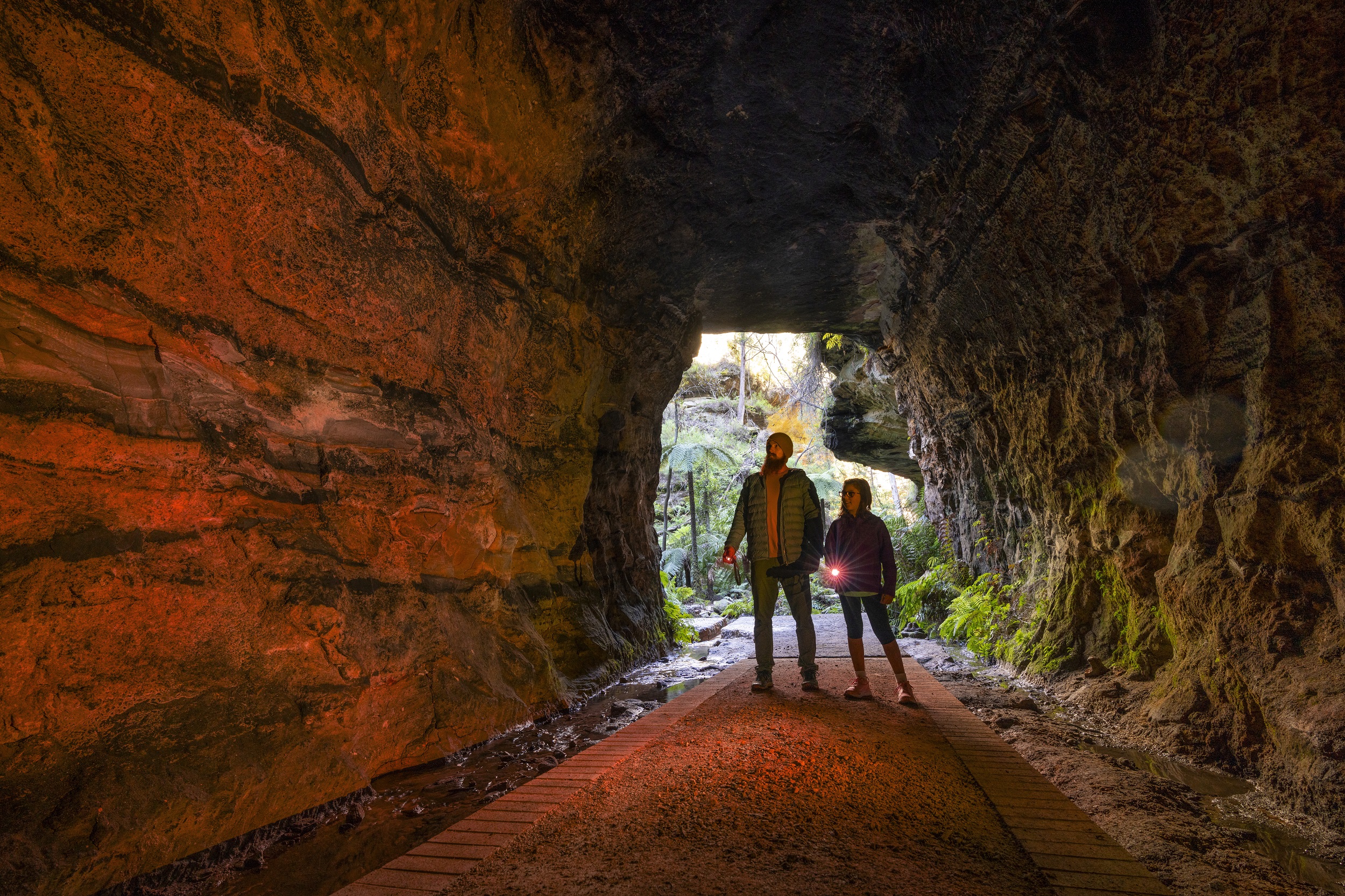 Two people just inside the entrance to Glow Worm Tunnel in Wollemi National Park. Photo credit: John Spencer/DCCEEW