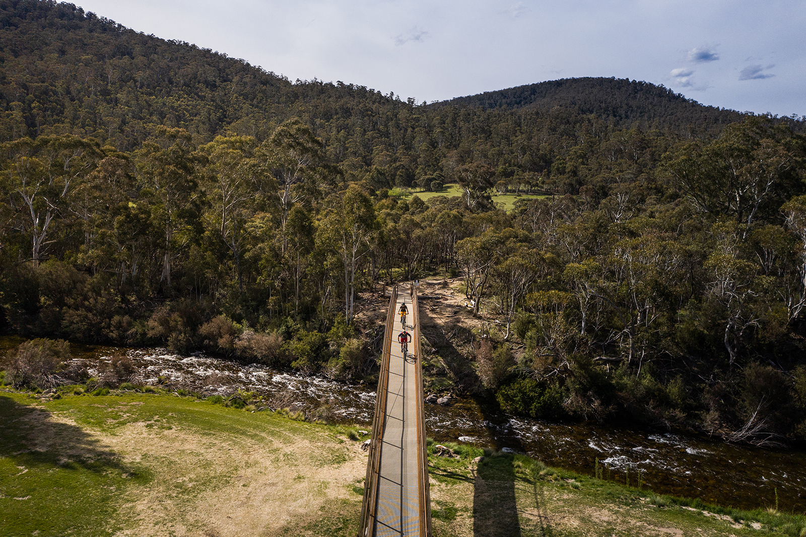 Aerial view of two guys riding the final bridge of the Lower Thredbo Valley track, Thredbo-Perisher area in Kosciuszko National Park. Photo credit: Rob Mulally/DPIE