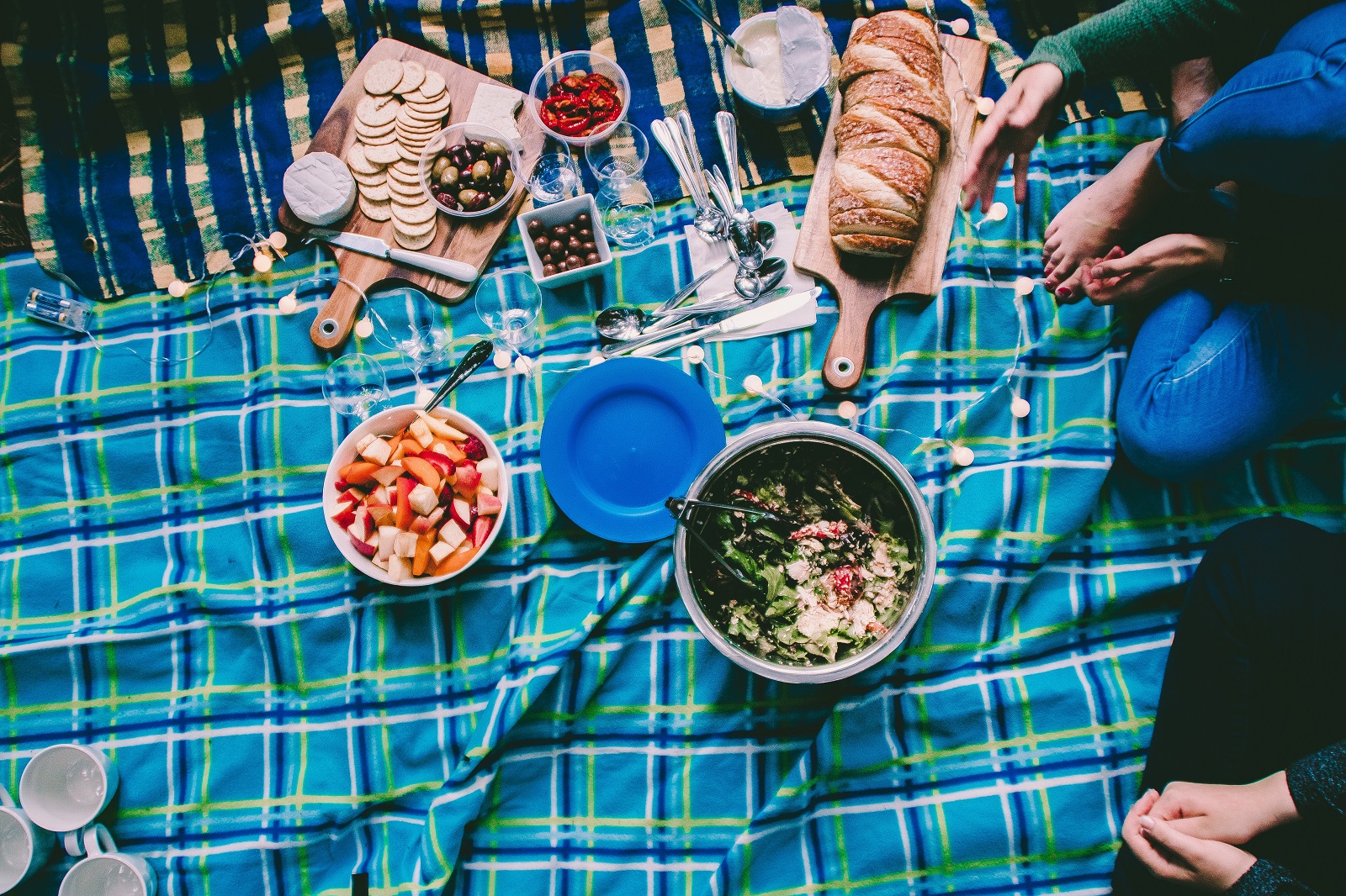 Looking down on a picnic of olives, sun dried tomatos, crackers, bread and salads on a picnic blanket. Photo: Brittany Gaiser/Unsplash