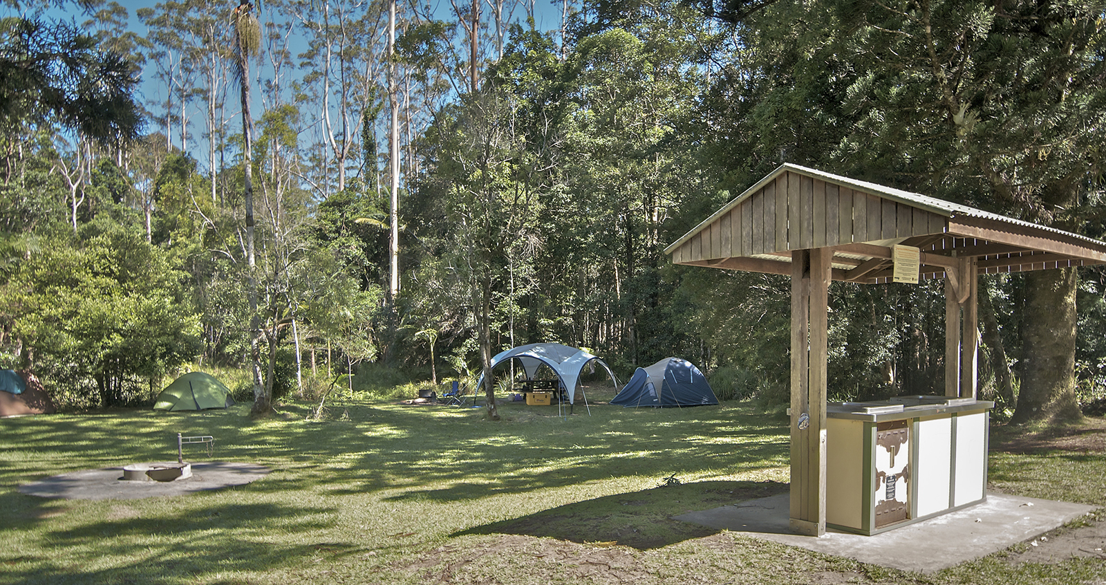 Rummery Park campground surrounded by bushland, showing covered barbecue, fire rings and tents, Whian Whian State Conservation Area. Photo: John Spencer/DPIE