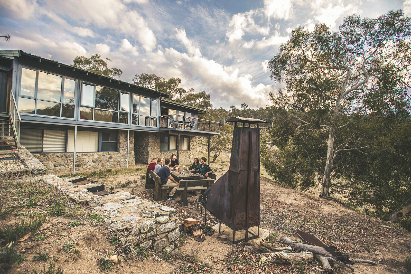 A group of people sitting outside near the outdoor fireplace at Creel Lodge, Thredbo-Perisher area in Kosciuszko National Park. Photo credit: Boen Ferguson/DPIE