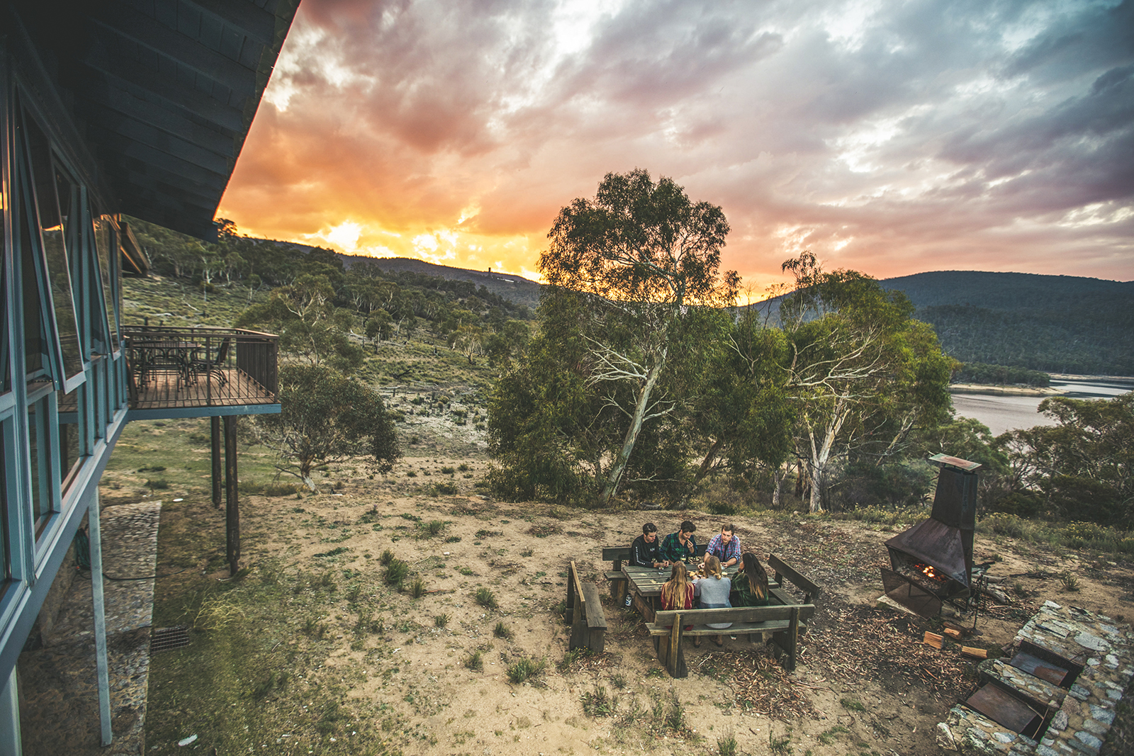 A group of people sitting outside near the outdoor fireplace at sunset at Creel Lodge, Thredbo-Perisher area in Kosciuszko National Park. Photo credit: Boen Ferguson/DPIE