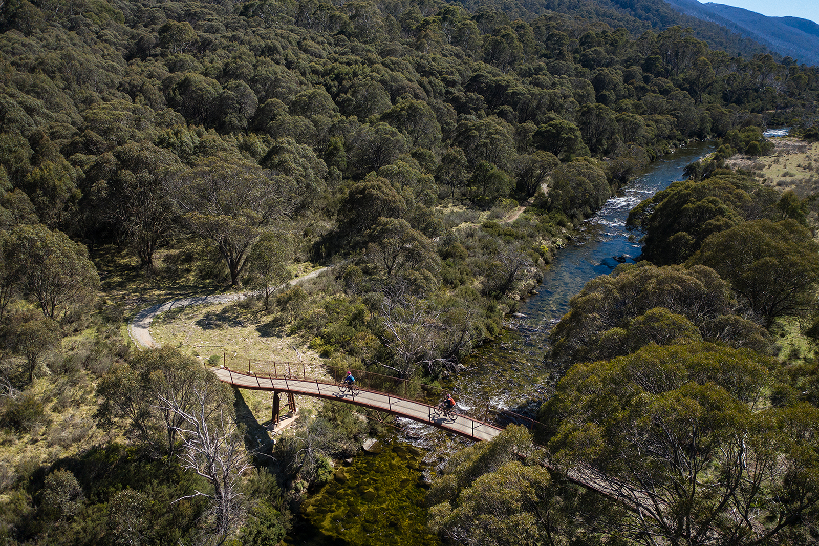 Aerial view of two people riding across a suspension bridge on the Thredbo Valley track. Photo credit: Rob Mulally/DPIE