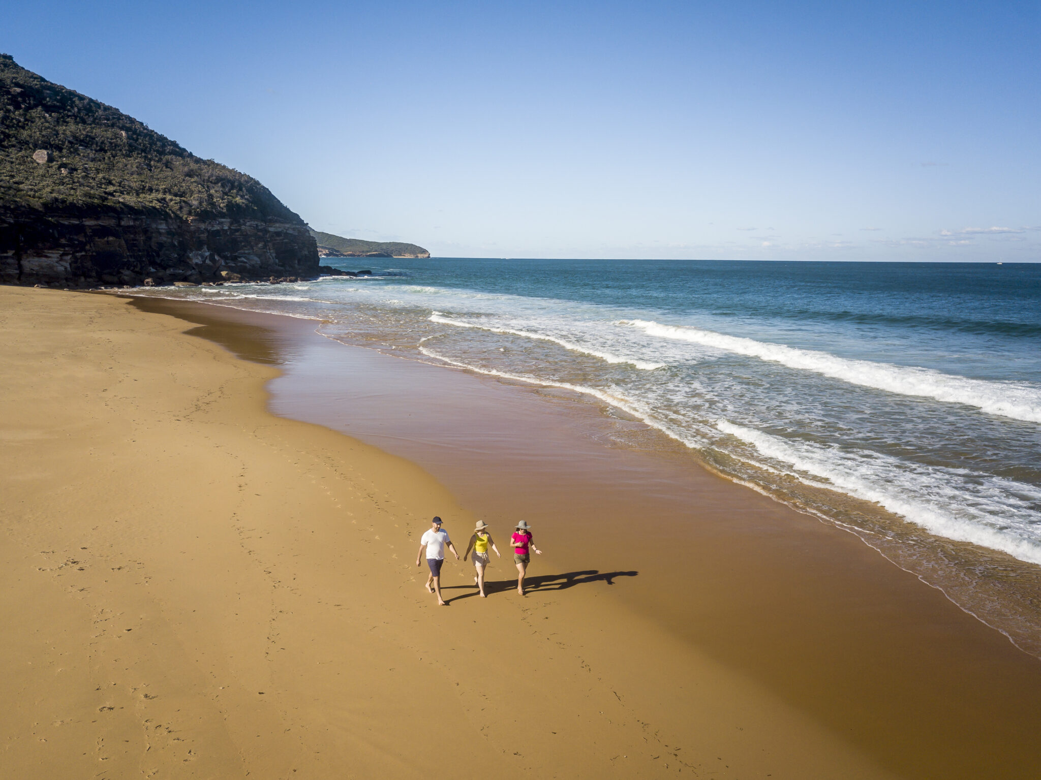 Aerial of three people walking along Tallow Beach, Bouddi National Park. Photo: John Spencer / DCCEEW © DCCEEW