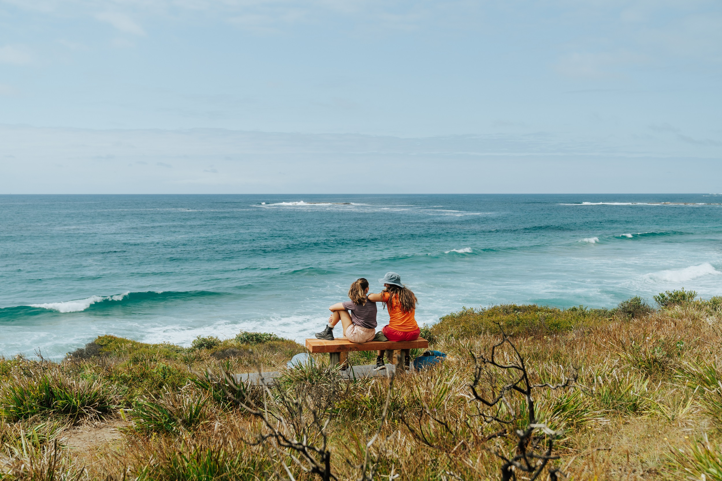 Two walkers sit to take in views of the ocean along the Murramarang South Coast Walk. Photo credit: Remy Brand/DCCEEW