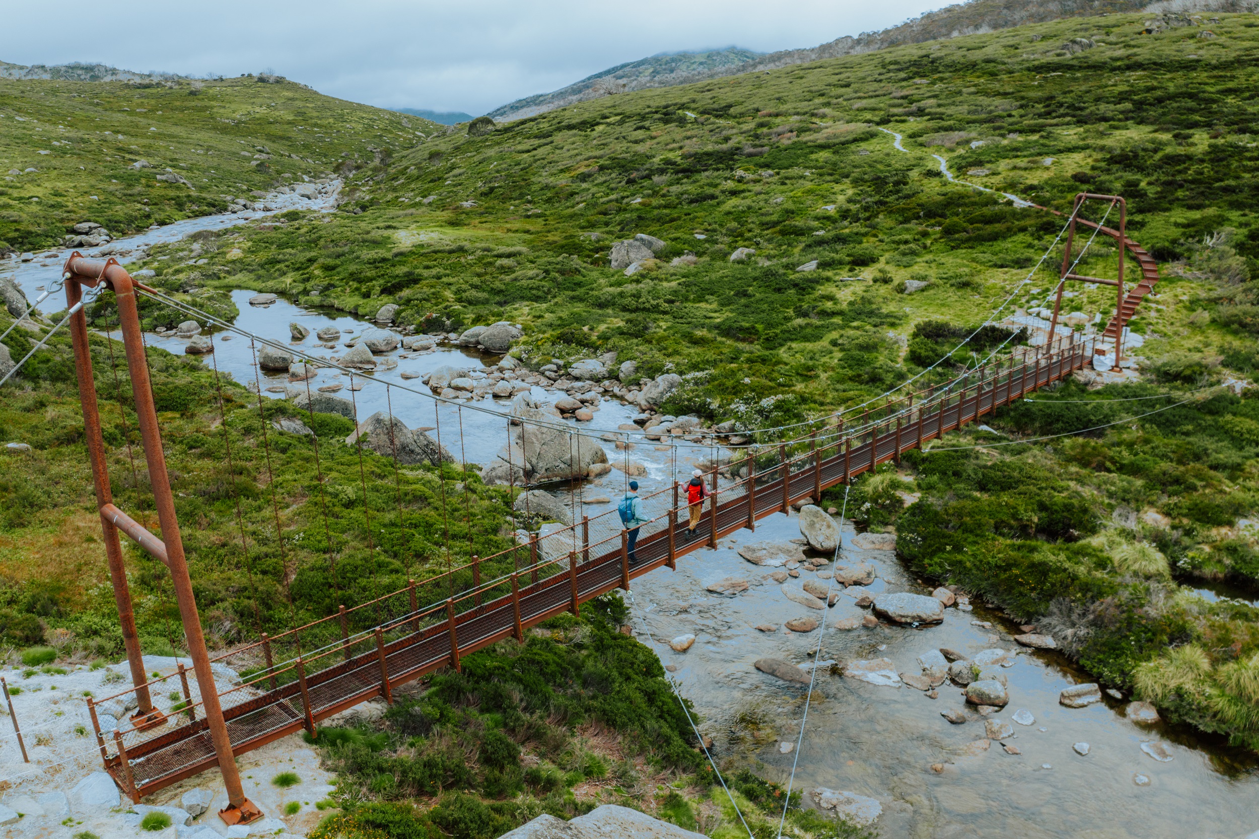 Two walkers cross Spencers Creek Suspension Bridge on the Snowies Alpine Walk. Photo: Daniel Parsons/DCCEEW © Studio Bilby