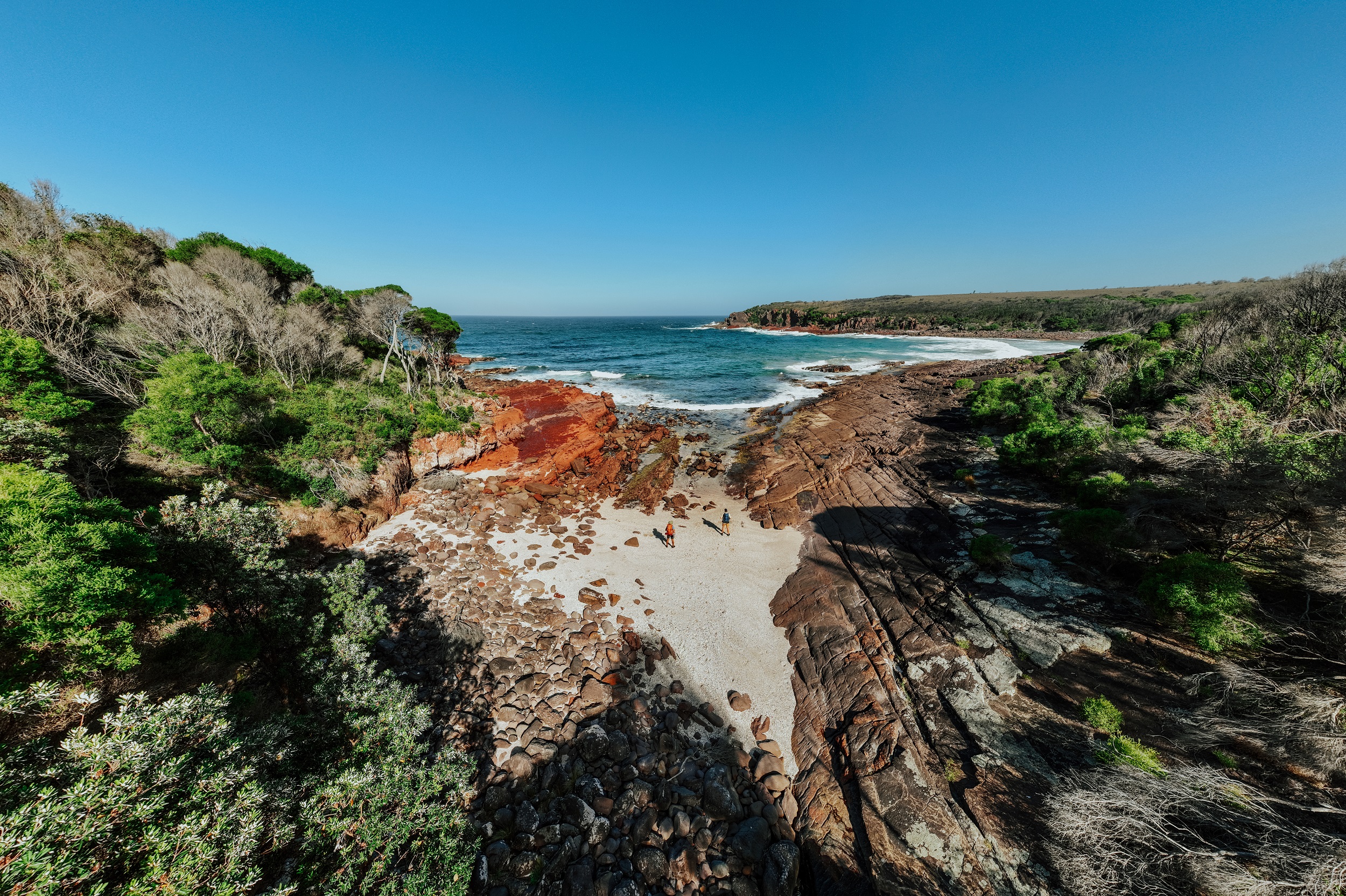 Two walkers at Hegartys Bay on the Light to Light Walk. Photo credit: Daniel Parsons/DCCEEW © Studio Bilby