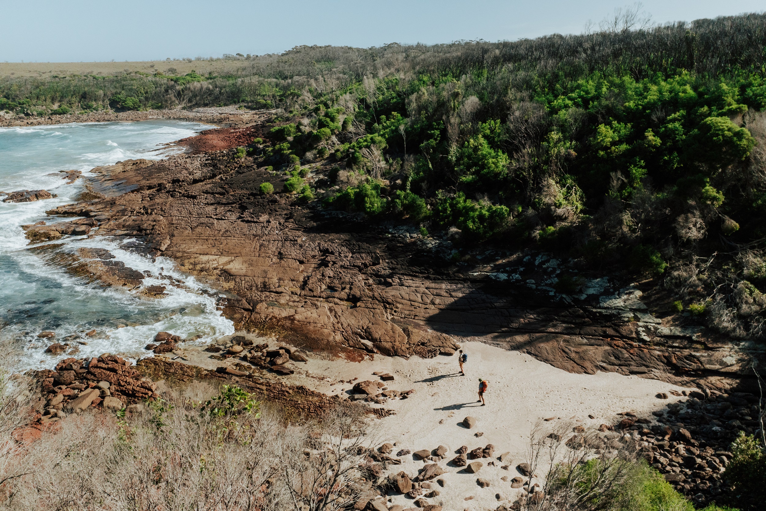 Two walkers at Hegartys Bay on the Light to Light Walk. Photo: Daniel Parsons / DCCEEW © Studio Bilby