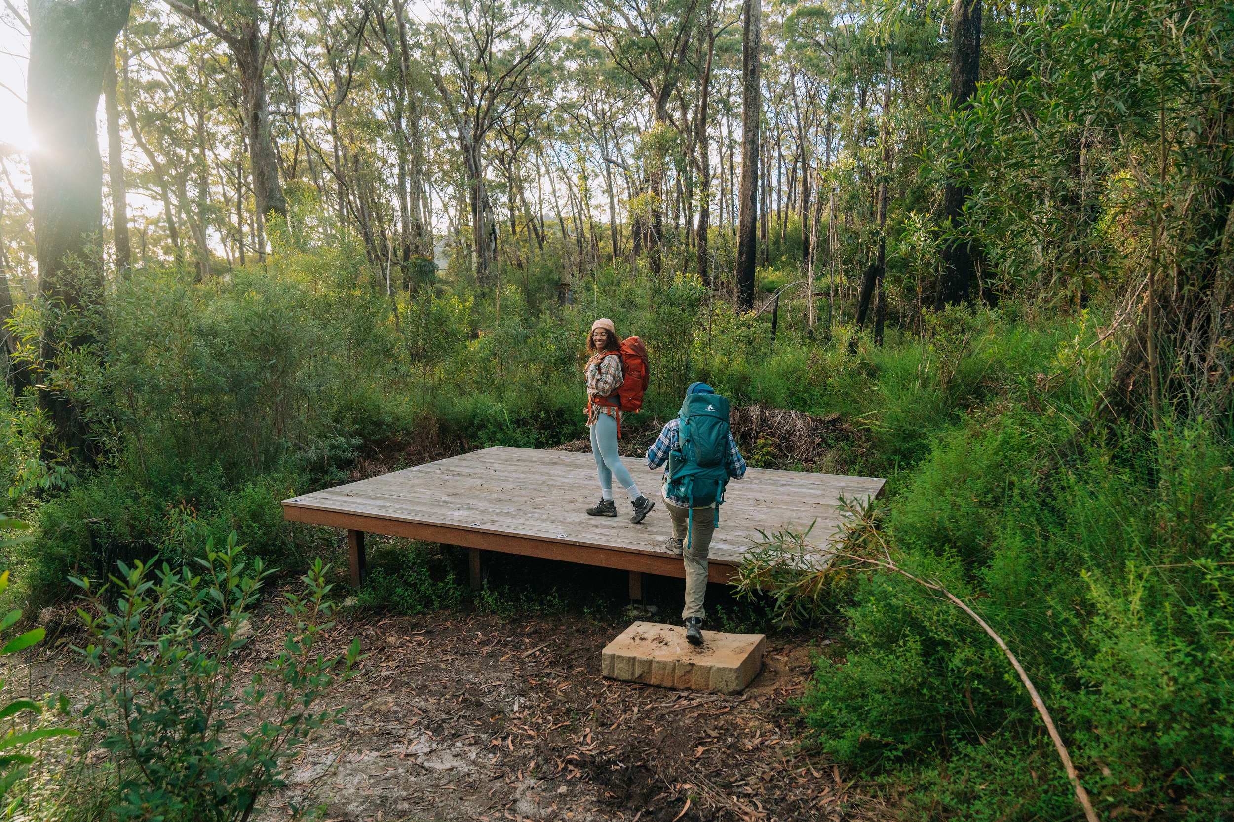 Two hikers walking onto a camping platform at Sand Ridge campground. Photo: Remy Brand/DCCEEW © Studio Bilby