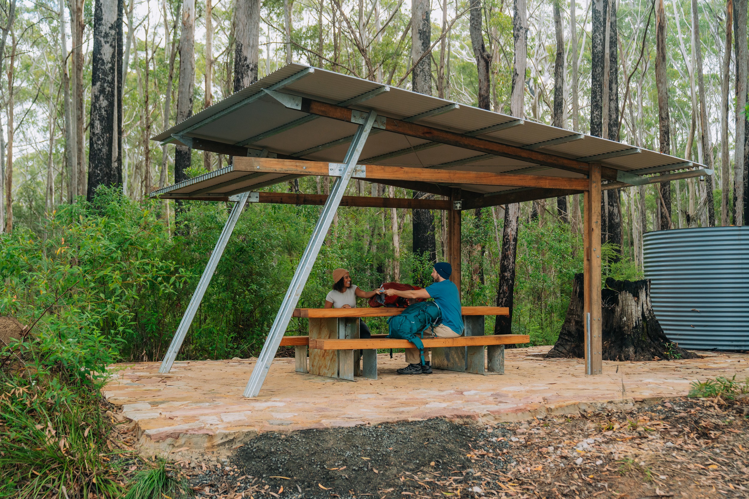 Two campers relax at a picnic table at Weeun Weeun campground on Gidjuum Gulganyi Walk. Photo: Remy Brand/DCCEEW © Studio Bilby