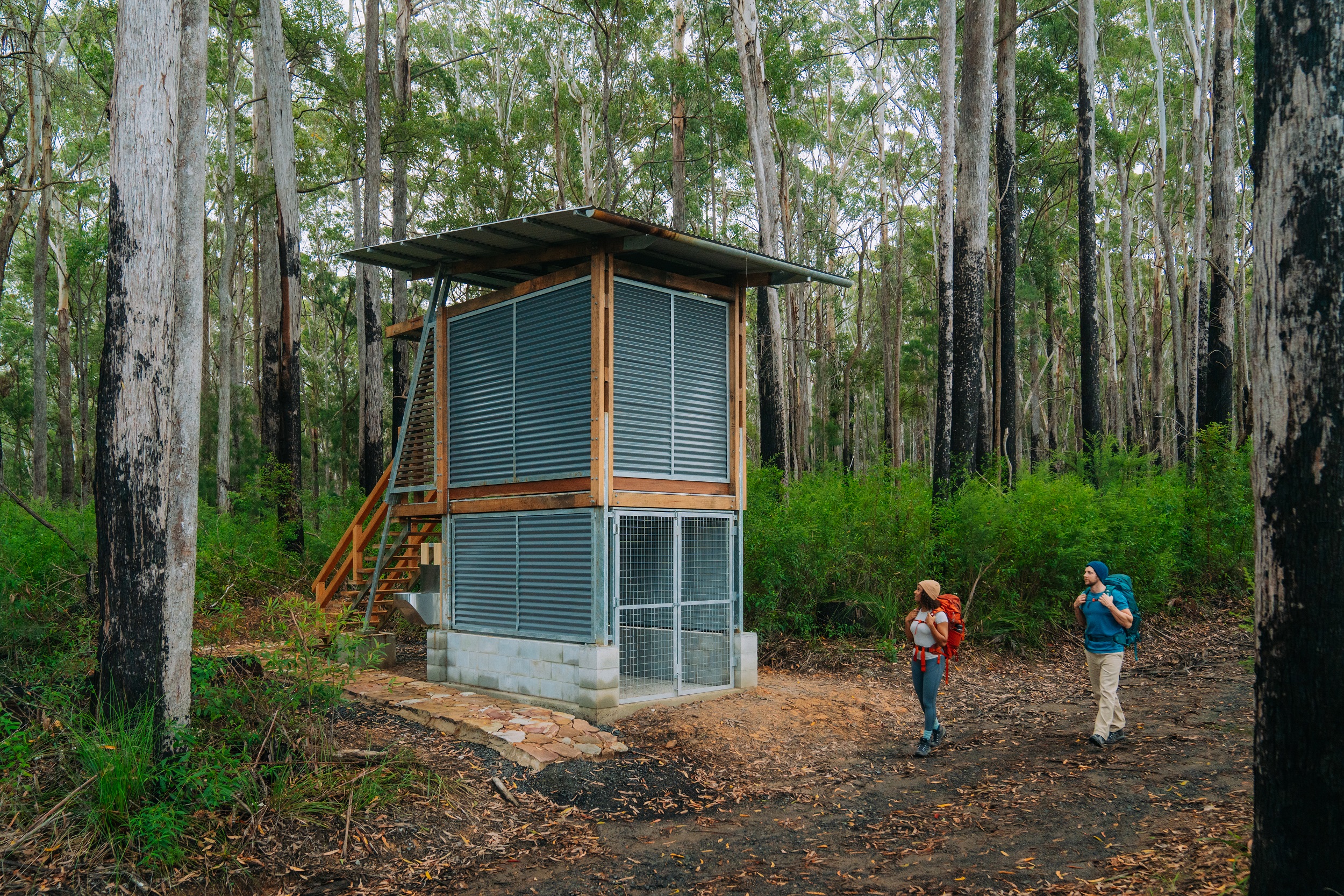 Two hikers passing an amenities building at Weeun Weeun campground on Gidjuum Gulganyi Walk. Photo: Remy Brand/DCCEEW © Studio Bilby