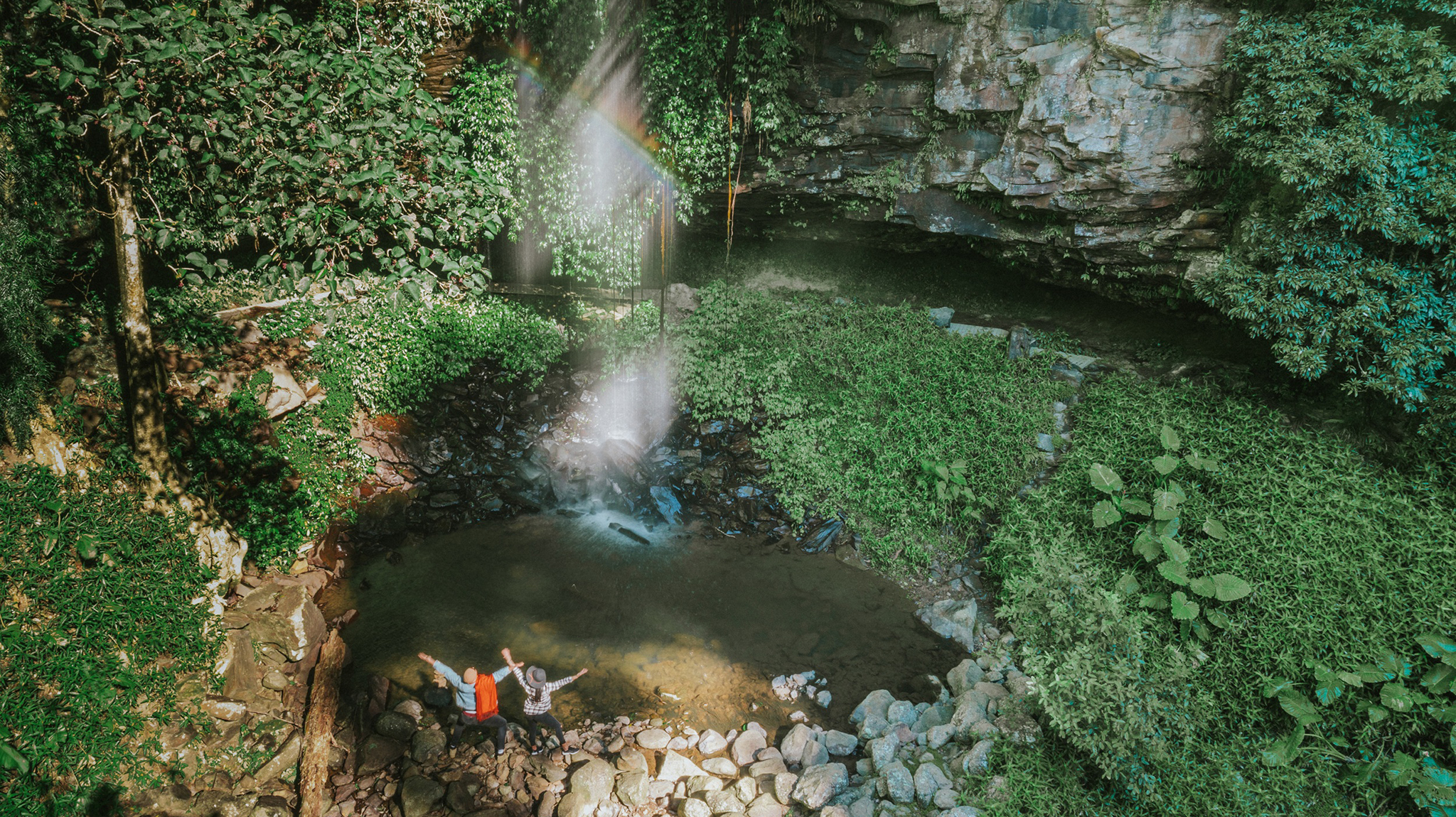 Two people at the base of a waterfall in Dorrigo National Park. Photo: Branden Bodman/DCCEEW © Studio Bilby