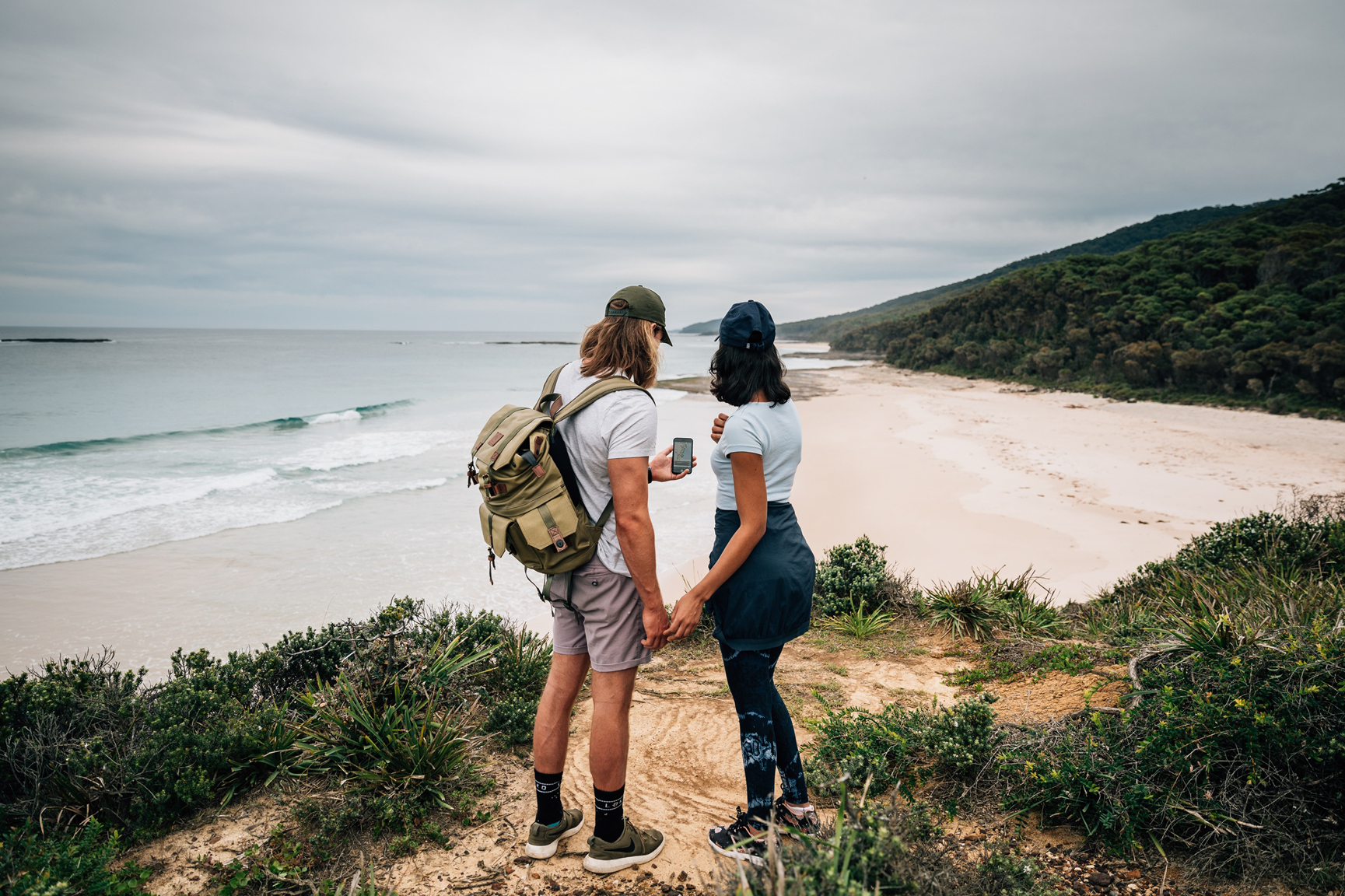 A couple looking checking the map on their phone as they follow a coastal track in Murramarang National Park. Photo: Melissa Findley/DCCEEW © Studio Bilby
