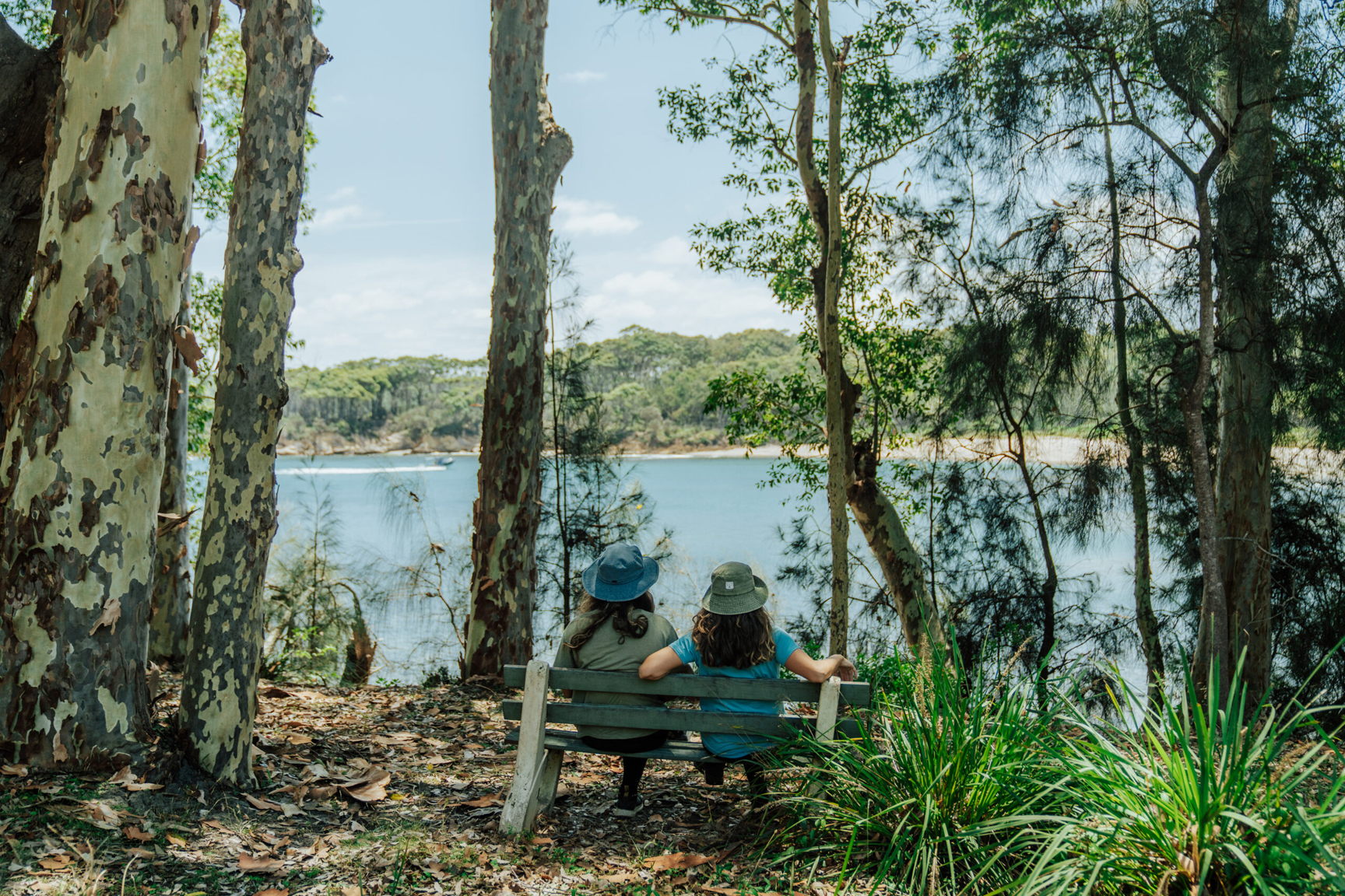 Two people sitting on a park bench overlooking the ocean in Murramarang National Park. Photo credit: Remy Brand/DCCEEW © Studio Bilby