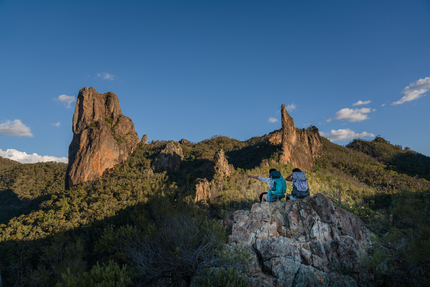 Two people sitting and looking at the Breadknife, Warrumbungle National Park. Photo: Rob Mulally / DCCEEW © Studio Bilby