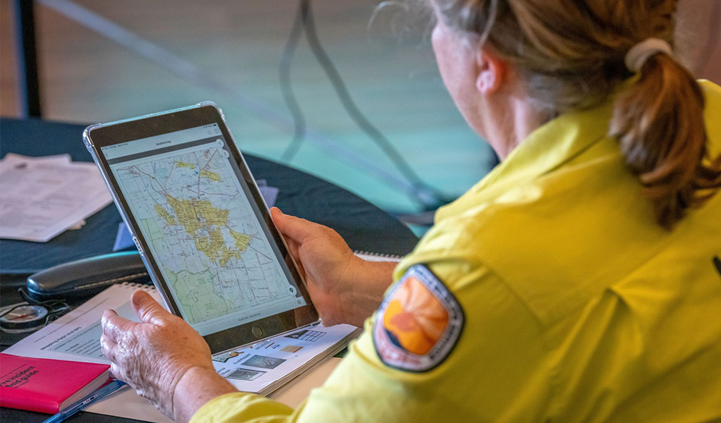 An NPWS staff member in uniform looking at a map in a training session. Credit: John Spencer &copy; DCCEEW