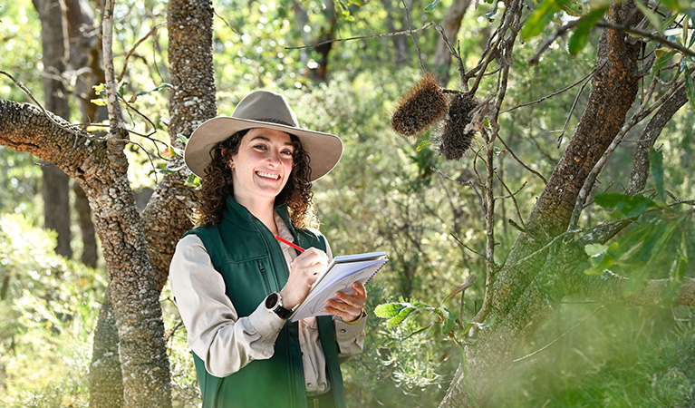 A woman in an NPWS uniform holding a pen and paper in a National Park. Credit: Adam Hollingworth/DCCEEW © DCCEEW