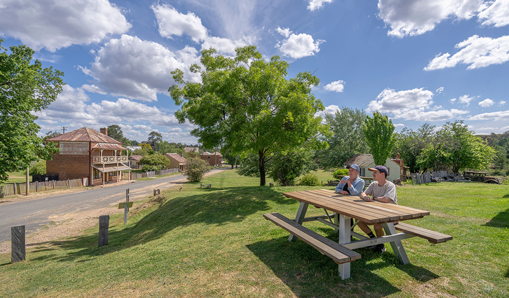Visitors sit in the idyllic surrounds of Hill End Historic Site, near its heritage buildings. Credit: John Spencer &copy; DCCEEW