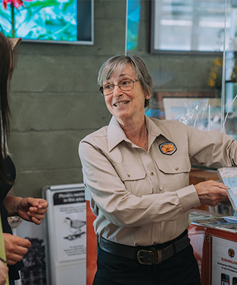 An NPWS staff member showing a visitor a map at a visitor's centre. Credit: Remy Brand &copy; DPE