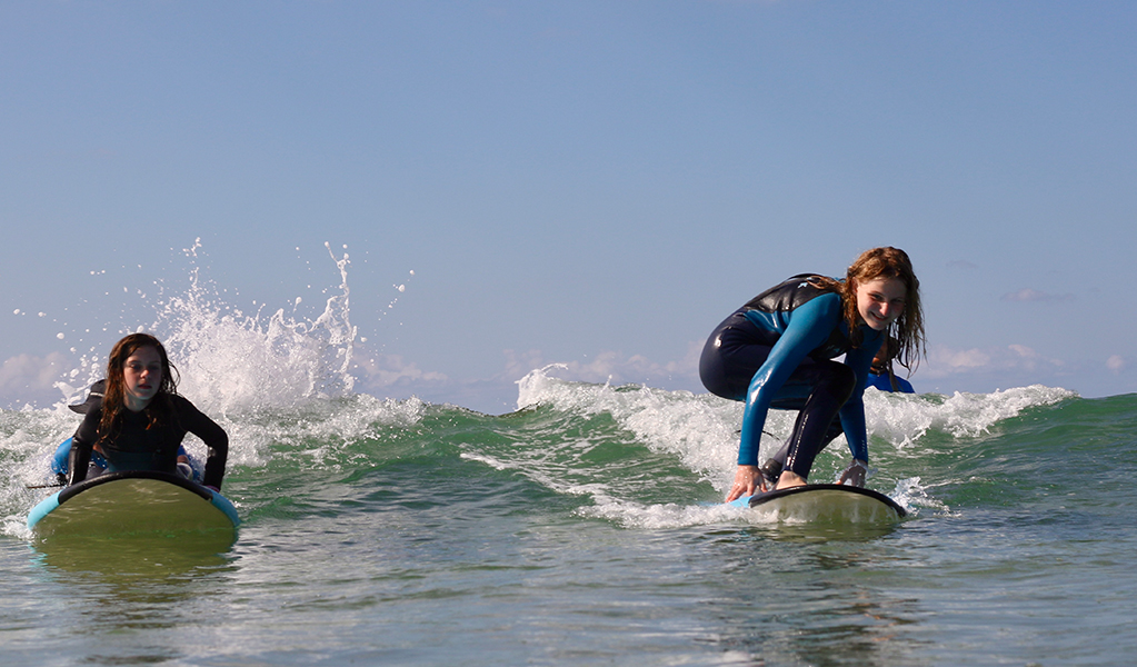 Two girls surfing in an accessible surf therapy lesson with Ability Surf. Credit: Grace Althorpe &copy; Ability Surf