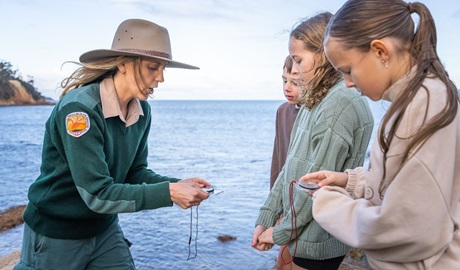 NPWS Ranger shows children a compass in Merimbula National Park. Photo: David Rogers &copy; DCCEEW