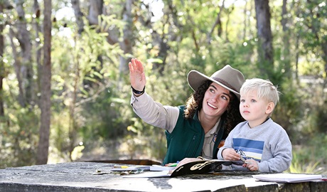 A discovery ranger looking through a book in the bush with a child on a tour in Warrumbungle National Park. Credit: Adam Hollingworth/DCCEEW &copy; DPE