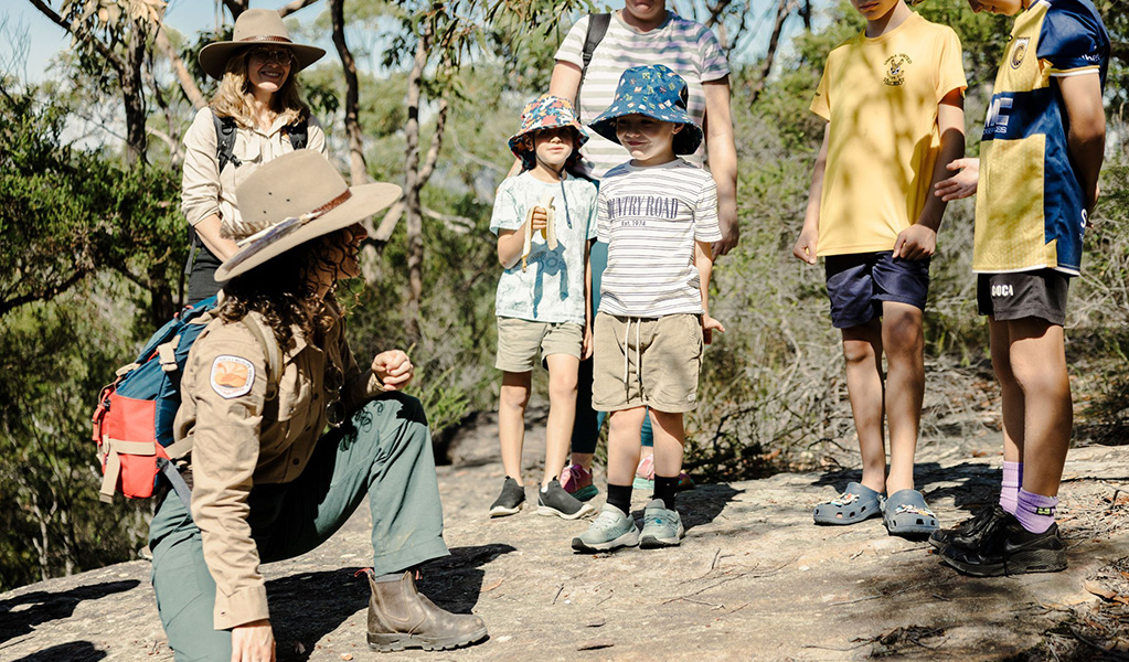 A Discovery ranger showing a group of kids through the bush on a guided tour. Credit &copy; Zain Kruyer/DCCEEW