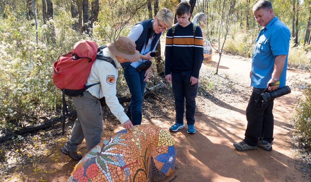 A park ranger showing a family the Pilliga Sculptures along the Sculptures in the Scrub walking track in the Pilliga Nature Reserve. Credit: Leah Pippos &copy; DPE