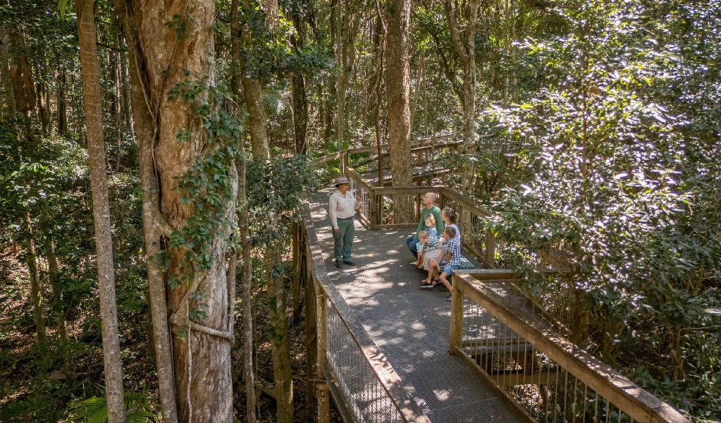 A family sitting on the boardwalk at Sea Acres National Park, listening to a Discovery ranger on a guided tour. Credit: John Spencer &copy; DCCEEW