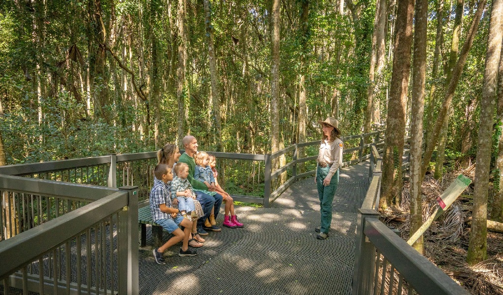 Family sitting, listening to a NPWS ranger on a guided tour of the Sea Acres National Park boardwalk. Credit: John Spencer &copy; DCCEEW