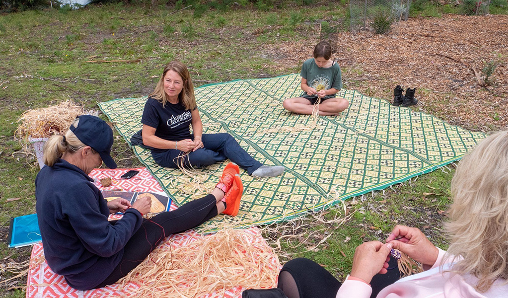 A group of people sitting on a woven rug participating in a traditional Aboriginal weaving workshop. Credit: &copy; Jessica Taunton/DCCEEW