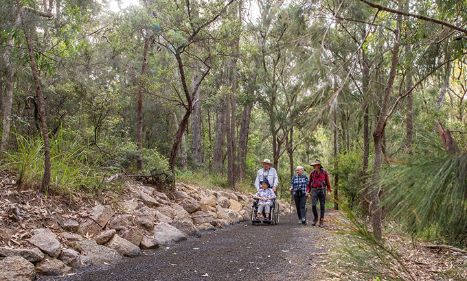 A group including a wheelchair user exploring the accessible Rockpools View walk in Boonoo Boonoo National Park. Credit: Simon Scott &copy; DCCEEW