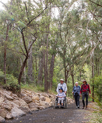 A group including a wheelchair user exploring the accessible Rockpools View walk in Boonoo Boonoo National Park. Credit: Simon Scott &copy; DCCEEW