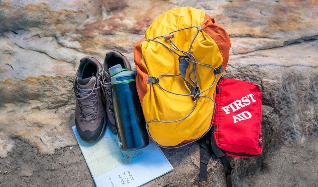 Backpack, first aid kit, water bottle, hiking shoes and map on a rock. Credit: John Spencer &copy; DCCEEW