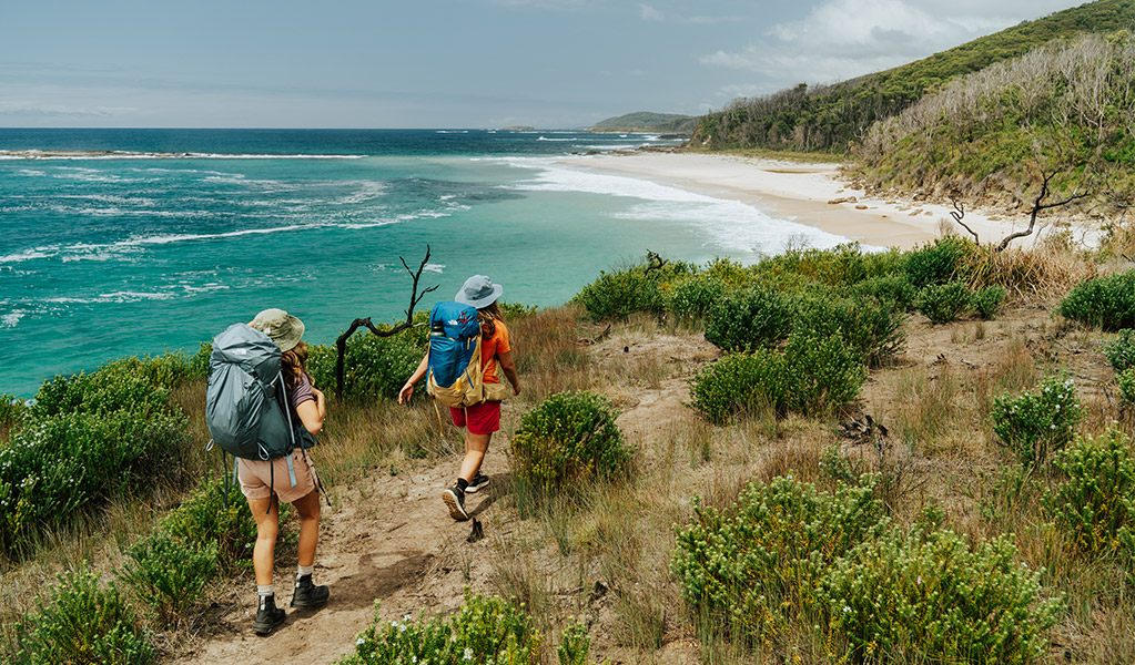 2 people on a walking track beside the ocean and bush along Murramarang South Coast Walk. Credit: Remy Brand &copy; Remy Brand