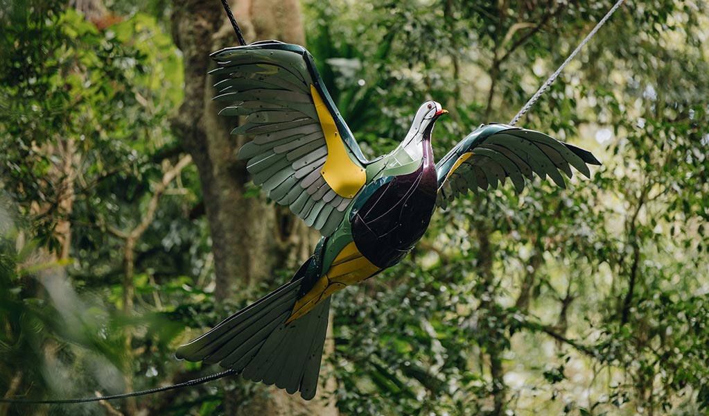 A painted sculpture of a wompoo fruit-dove in flight hangs amongst trees at Dorrigo Rainforest. Photo: Jay Black &copy; DPE
