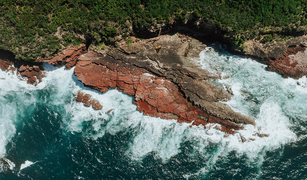 Waves crashing over the red rocks near Saltwater Beach. Credit: Daniel Parsons/DCCEEW &copy; Daniel Parsons