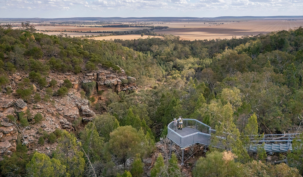 Two women stand at the steel railing of Jacks Creek lookout with views down into a gorge and expansive views out across country. Credit: John Spencer &copy; DCCEEW