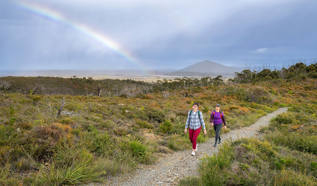 2 hikers on Diamond Head loop walk with Three Brothers mountains and a rainbow in the background. Credit: John Spencer &copy; DCCEEW