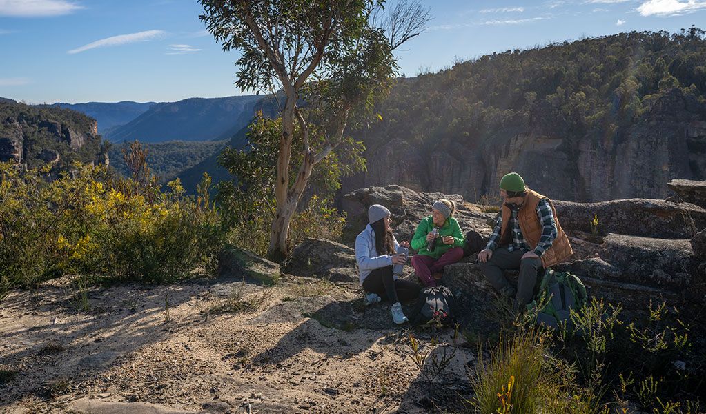 3 people sitting at Carne View lookout along Broad Swamp to Birds Rock walking track. Credit: John Spencer &copy; DCCEEW