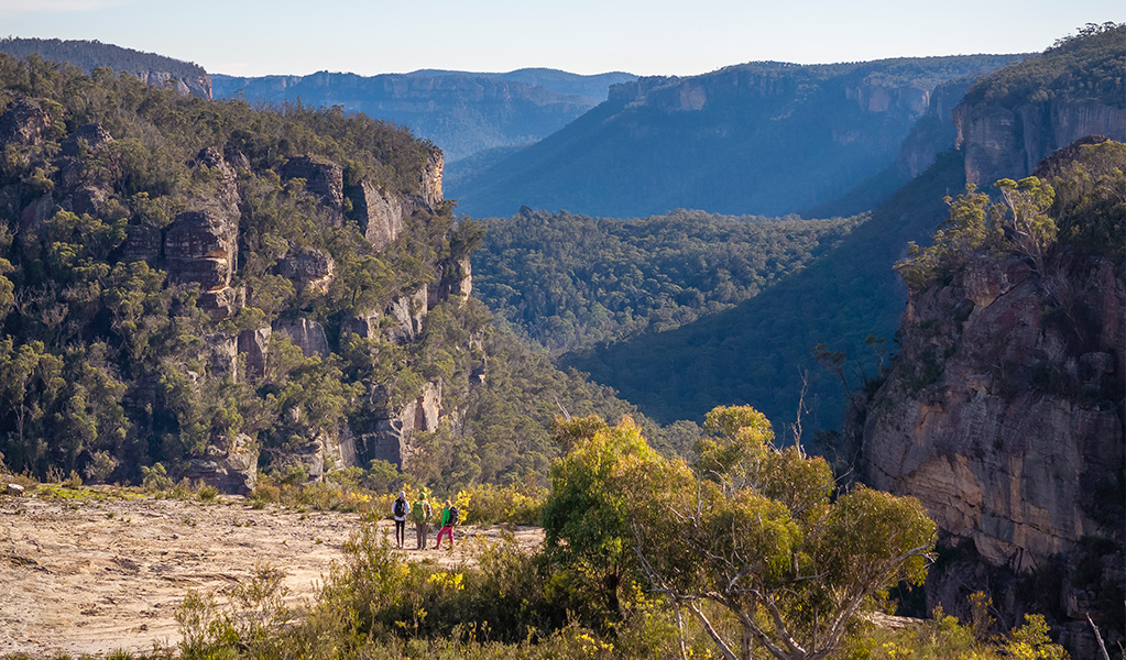 An aerial view of 3 hikers enjoying the view from Carne View lookout along Broad Swamp to Birds Rock walking track in Gardens of Stone State Conservation Area. Credit: John Spencer &copy; DCCEEW