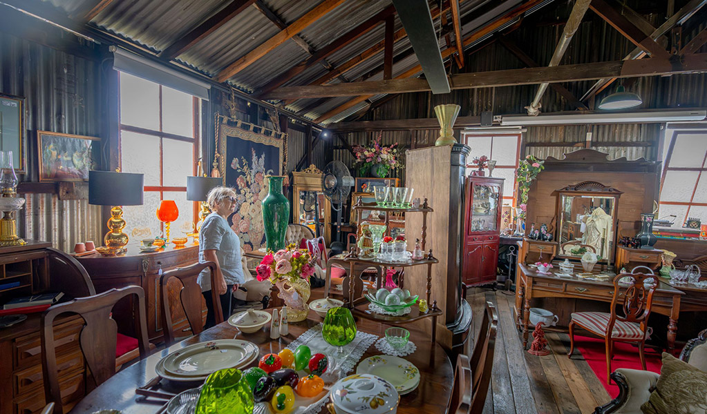 A visitor looking at an antique green vase surrounded by antiques for sale at Gold Rush Antiques store in Hartley Historic Site. Credit: John Spencer &copy; DCCEEW
