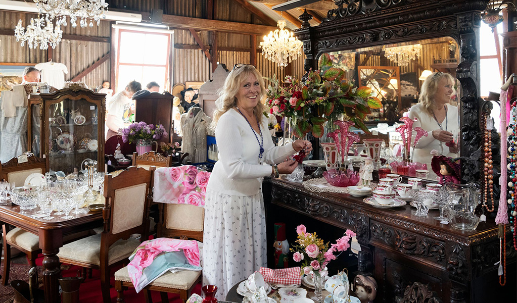 A woman standing among homewares at Gold Rush Antiques in Hartley Historic Site. Credit: Ben Pearse &copy; DCCEEW