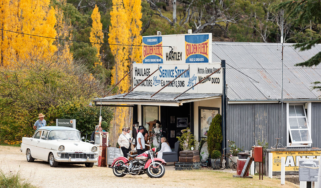 People, vintage cars and motorbikes out the front of Gold Rush Antiques in Hartley Historic Site. Credit: Ben Pearse &copy; DCCEEW