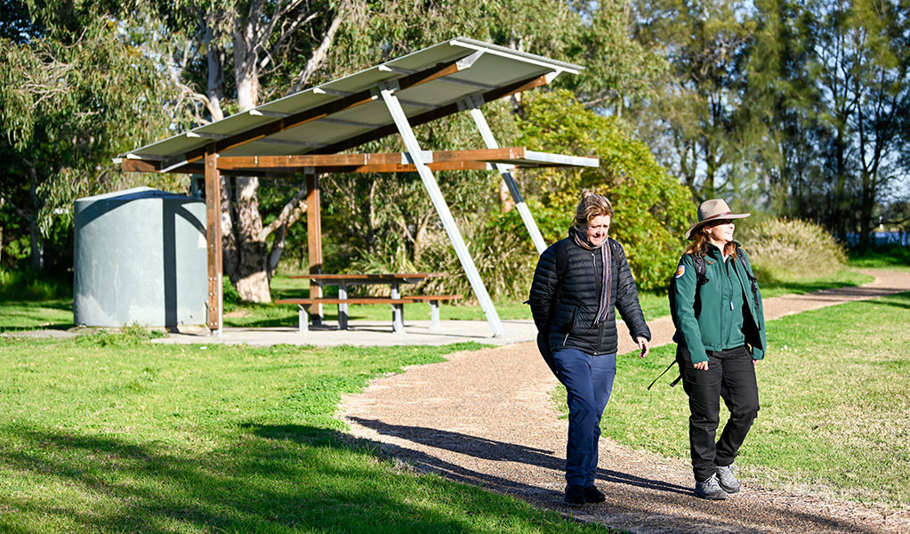 A ranger and a visitor walking past a sheltered picnic table in Hunter Wetlands National Park. Credit: Adam Hollingworth &copy; DCCEEW