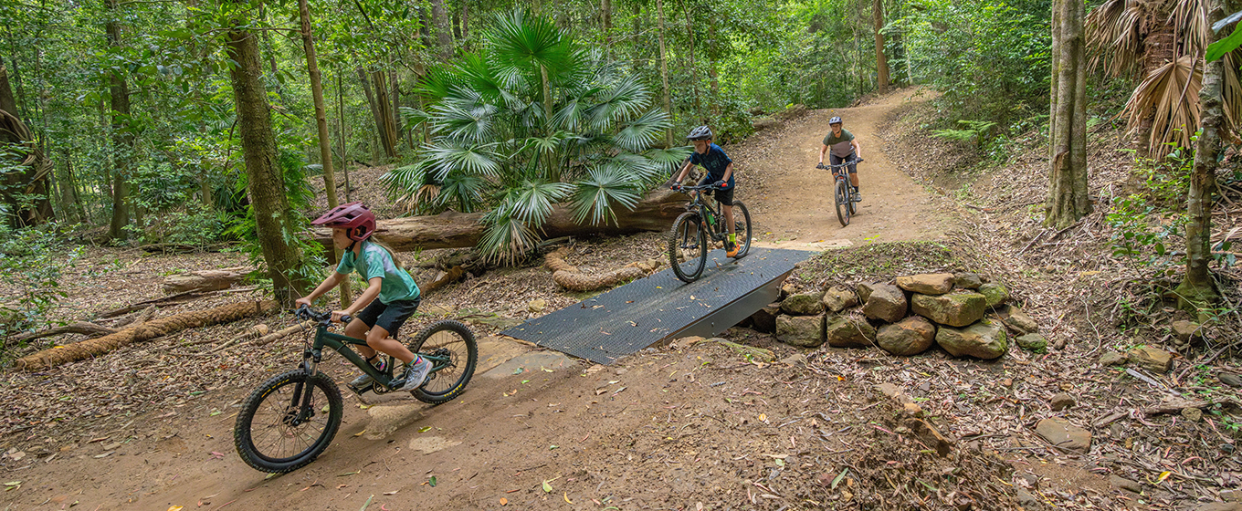 Three young kids ride across a mesh bridge on Kembla mountain bike trails. Credit: John Spencer &copy; DCCEEW