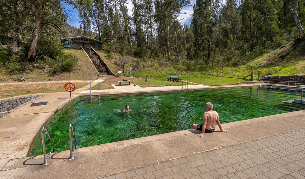 Two people at Yarrangobilly Caves thermal pool with a staircase leading to a toilet block in the background. Credit: John Spencer &copy; DCCEEW