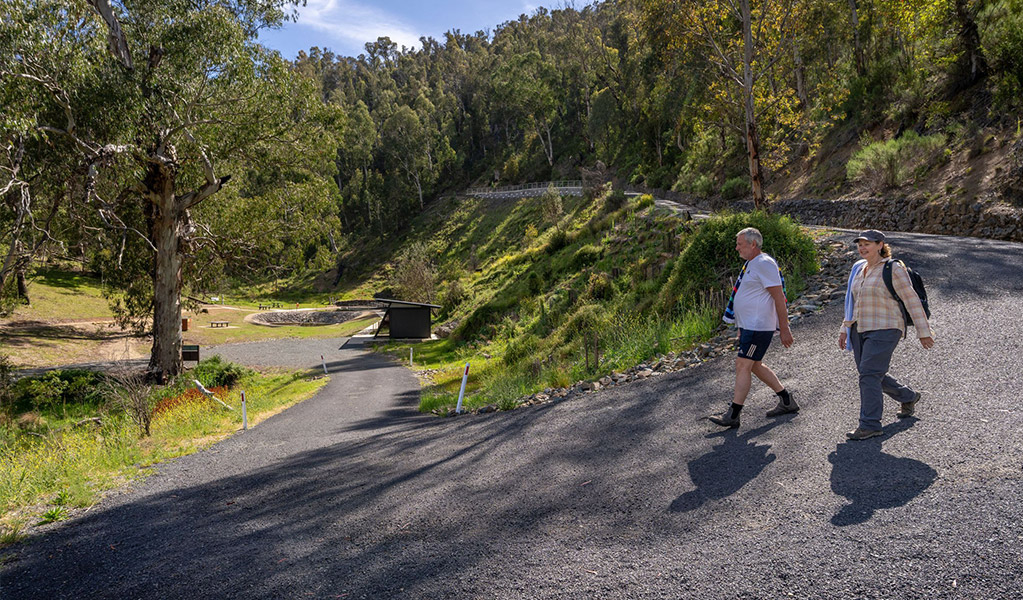 Two people walking down Yarrangobilly Thermal Pool walk, a short but steep bitumen road down to the pool. Credit: John Spencer &copy; DCCEEW