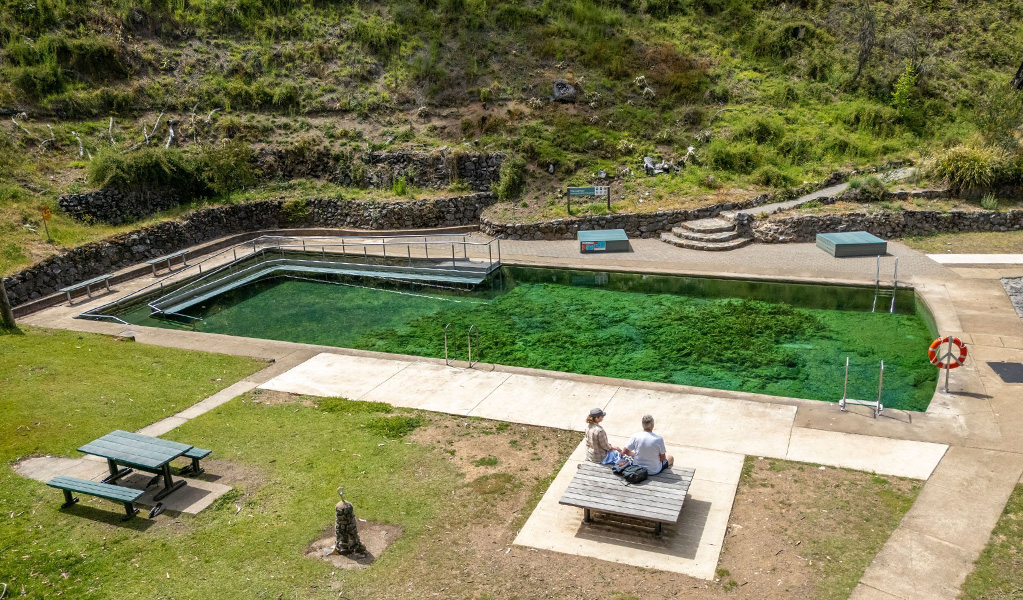 Two people sitting on a platform bench next to Yarrangobilly Caves Thermal Pool fed by a natural spring. Credit: John Spencer &copy; DCCEEW