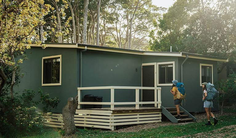 2 walkers climbing the steps to their hard-roof accommodation at Depot Beach cabins, Murramarang National Park. Photo: Remy Brand &copy; Remy Brand